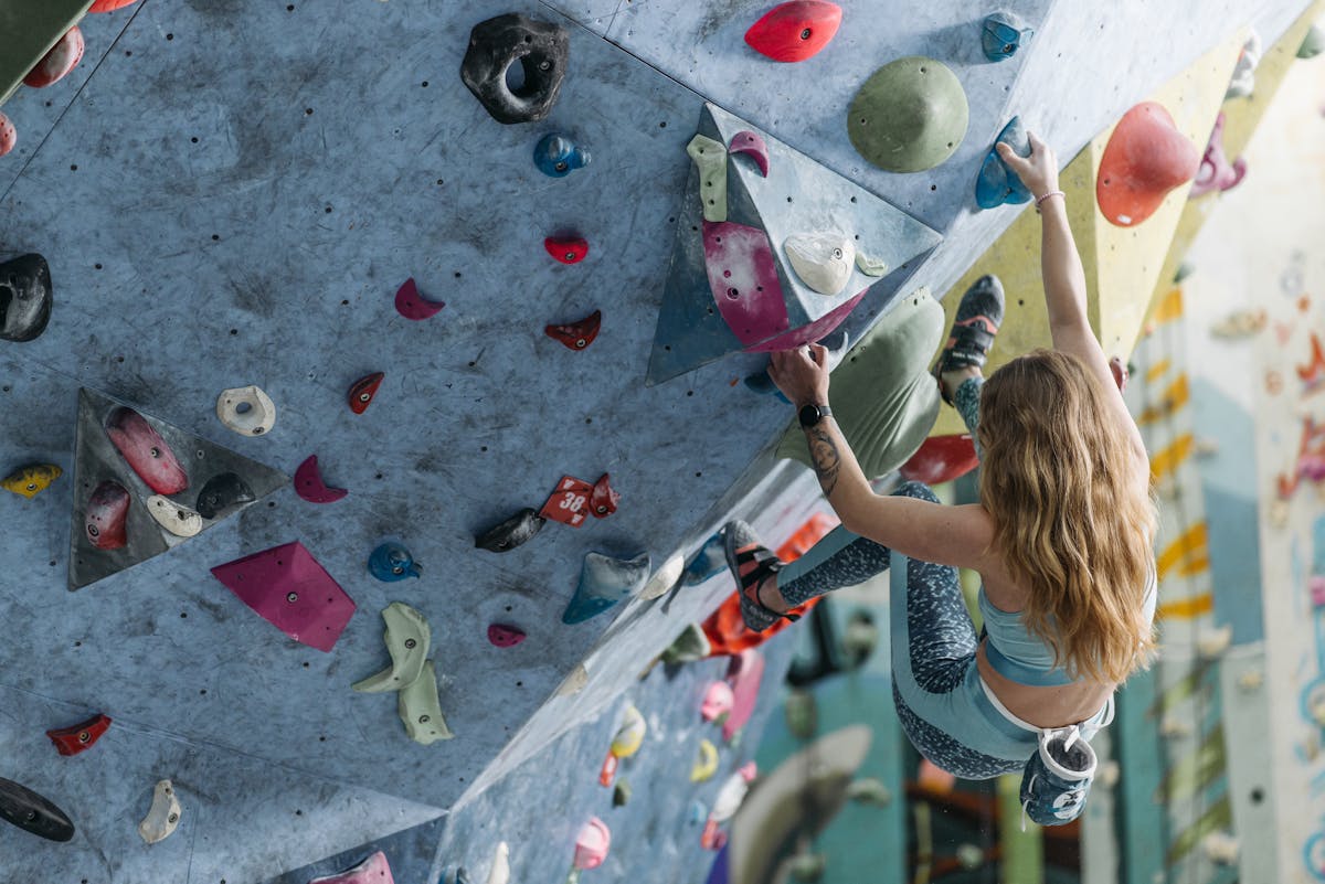 A woman climbing a colorful bouldering wall indoors, showcasing strength and agility.