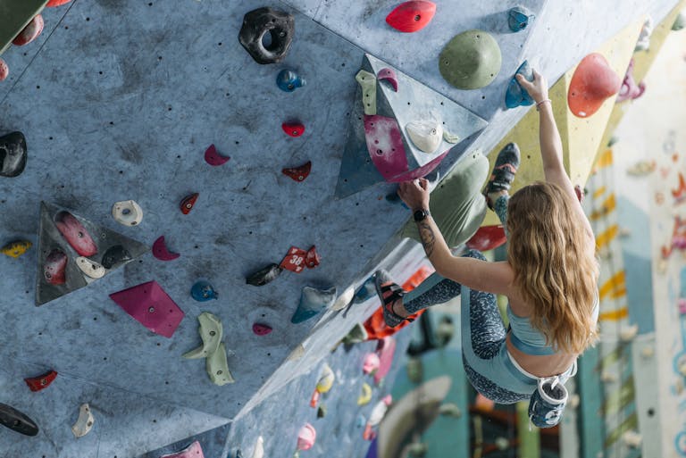 A woman climbing a colorful bouldering wall indoors, showcasing strength and agility.