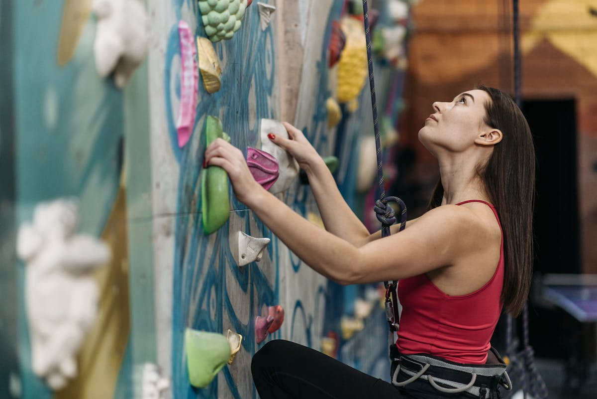 Young woman scaling an indoor climbing wall with colorful grips and harness.